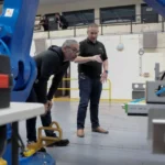 two workers working on something with a nano-heat on the wall in the background.