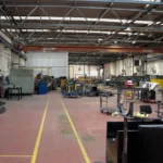 a warehouse with 9 x-heat heaters in view, most of them are one the right wall, which is white and made out of bricks.
